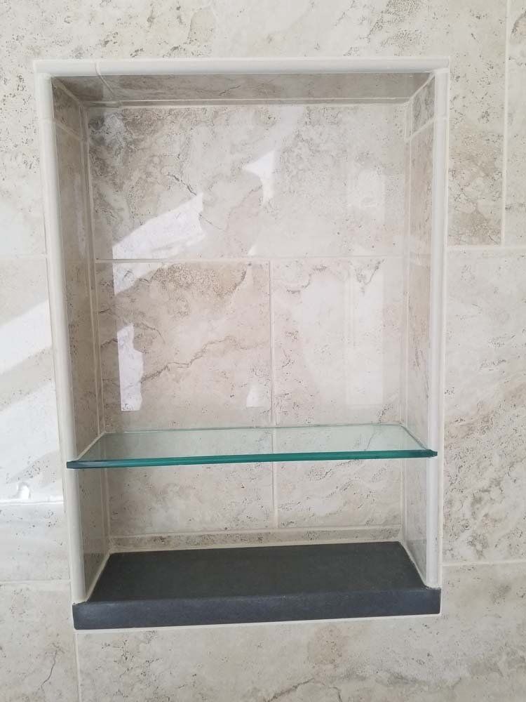 Built-in shower niche with a glass shelf, set in beige and gray tiled wall.