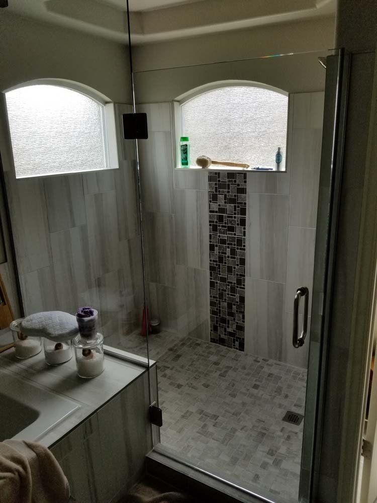 Bathroom with walk-in shower. Gray and white tiles. Glass door. Arched windows above shower.