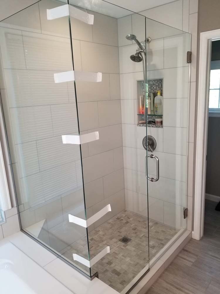 Glass-enclosed shower with white tiled walls, pebble floor, and built-in niche for toiletries.