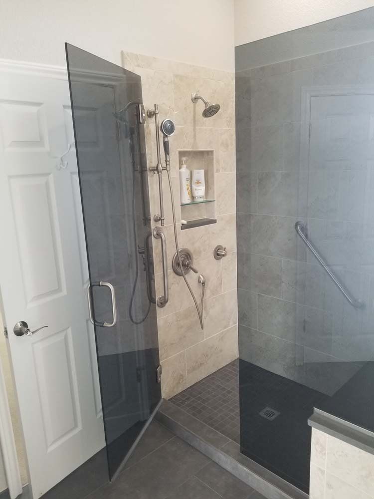 Shower with a glass door, light beige and gray tile, and a grab bar.