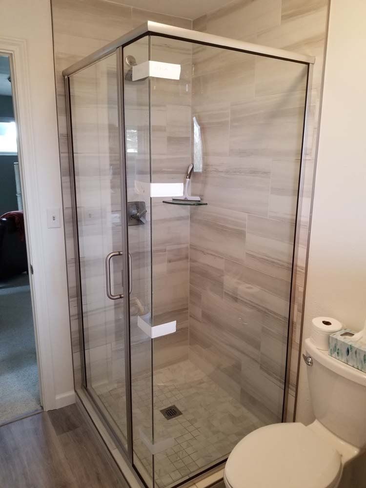 Glass shower enclosure with gray tile walls, in a bathroom. Toilet is adjacent.