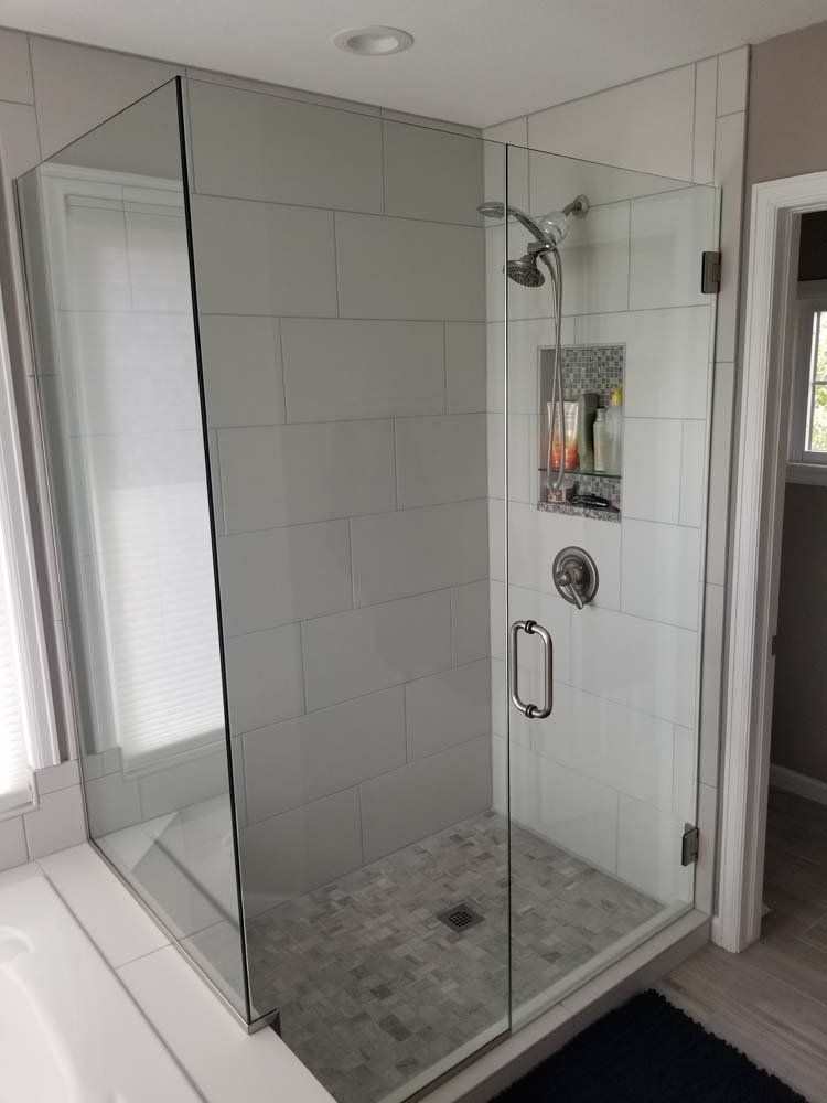 Glass-enclosed shower with white tiled walls, silver fixtures, and a gray stone floor.