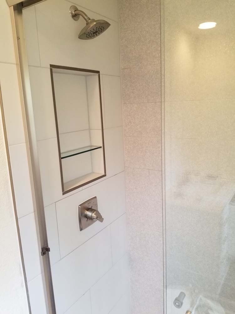 Shower with white tiles, brushed nickel fixtures, built-in shelf, and glass door.