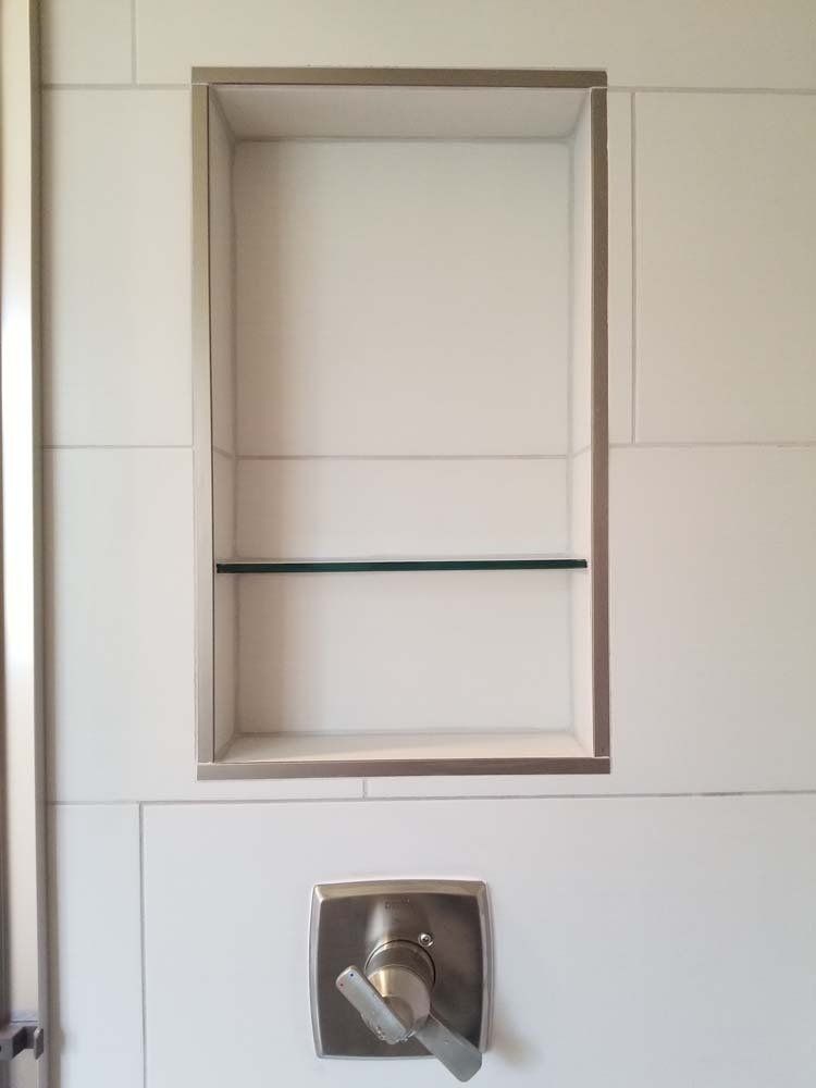 White tiled shower wall with recessed shelf and faucet.