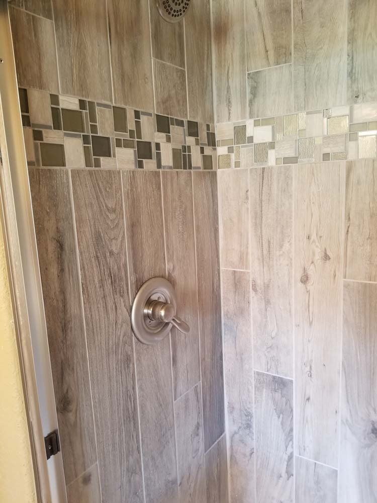 Shower interior with gray wood-look tiles, mosaic accent strip, and silver faucet.