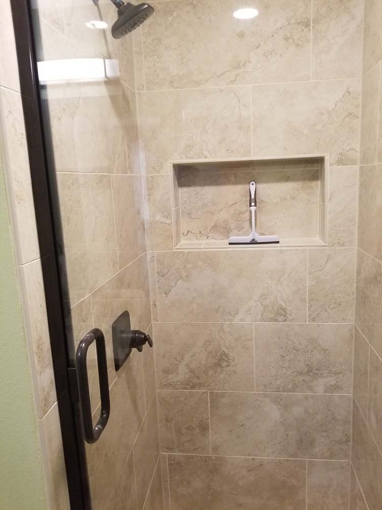 Shower with beige tile walls, glass door, and niche with a squeegee.