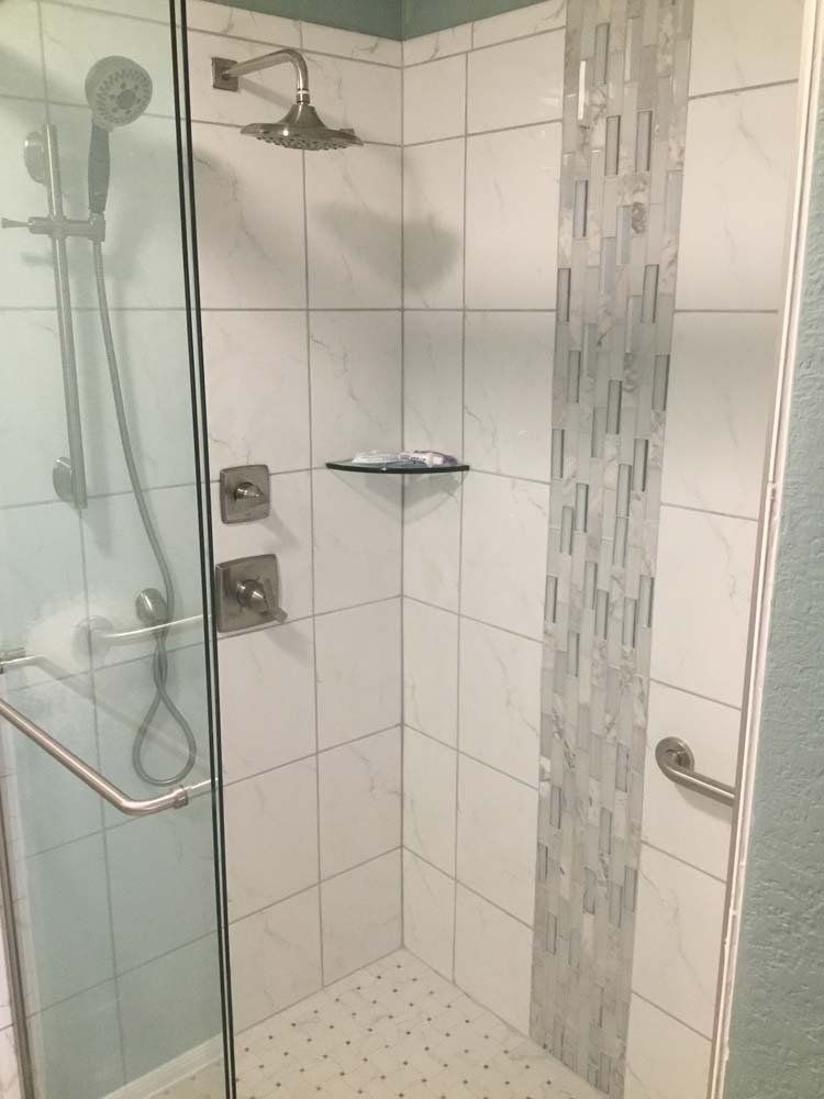 Bathroom shower with glass door, white tile, accent strip, and grab bar.