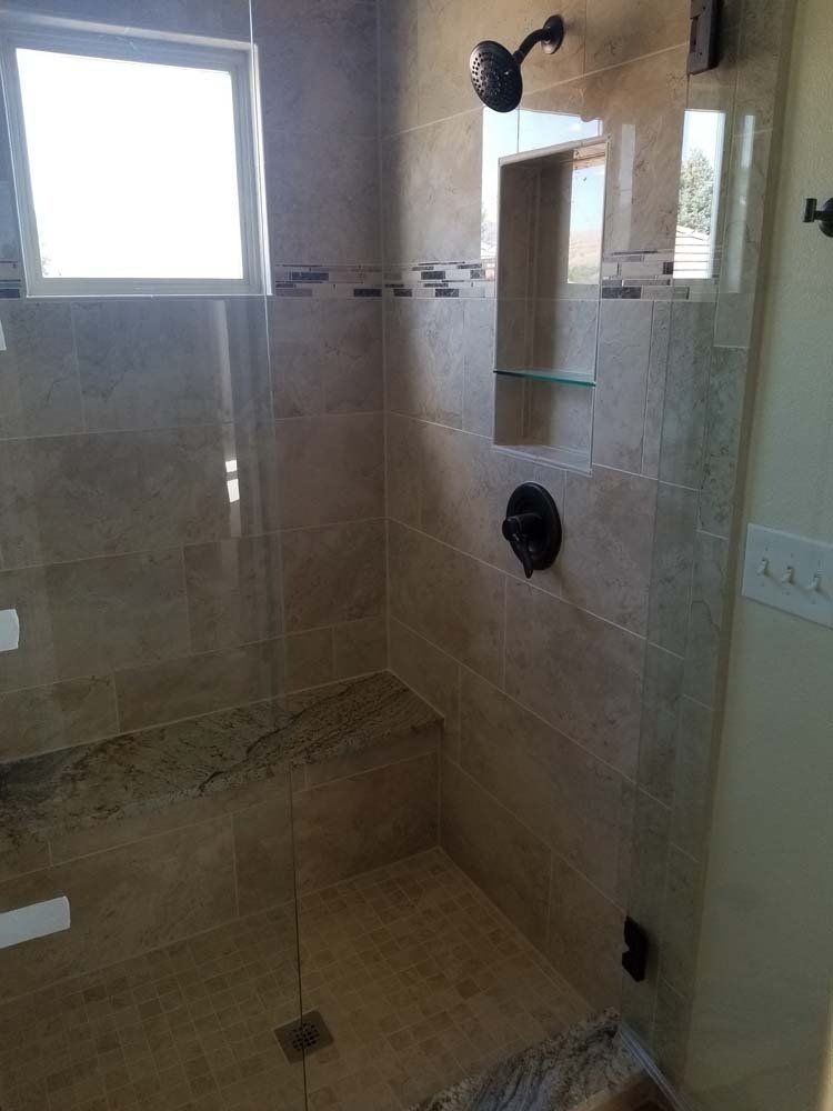 Tiled shower stall with a built-in bench, glass shelf, and dark shower fixtures.