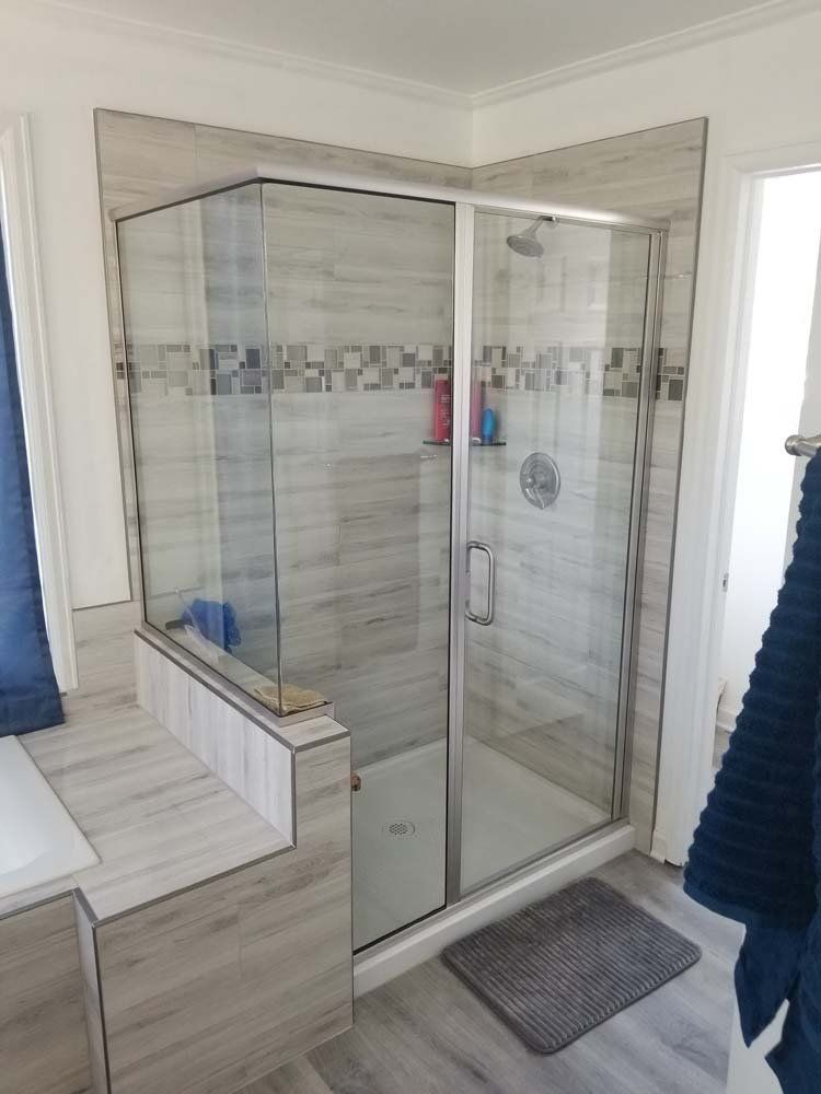 A corner glass shower with light gray tile and a decorative band, next to a step-up and towel bar.