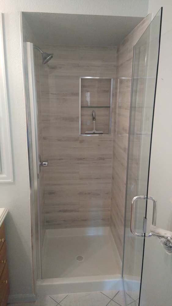 Shower with glass door, white tiled walls, and a built-in shelf.