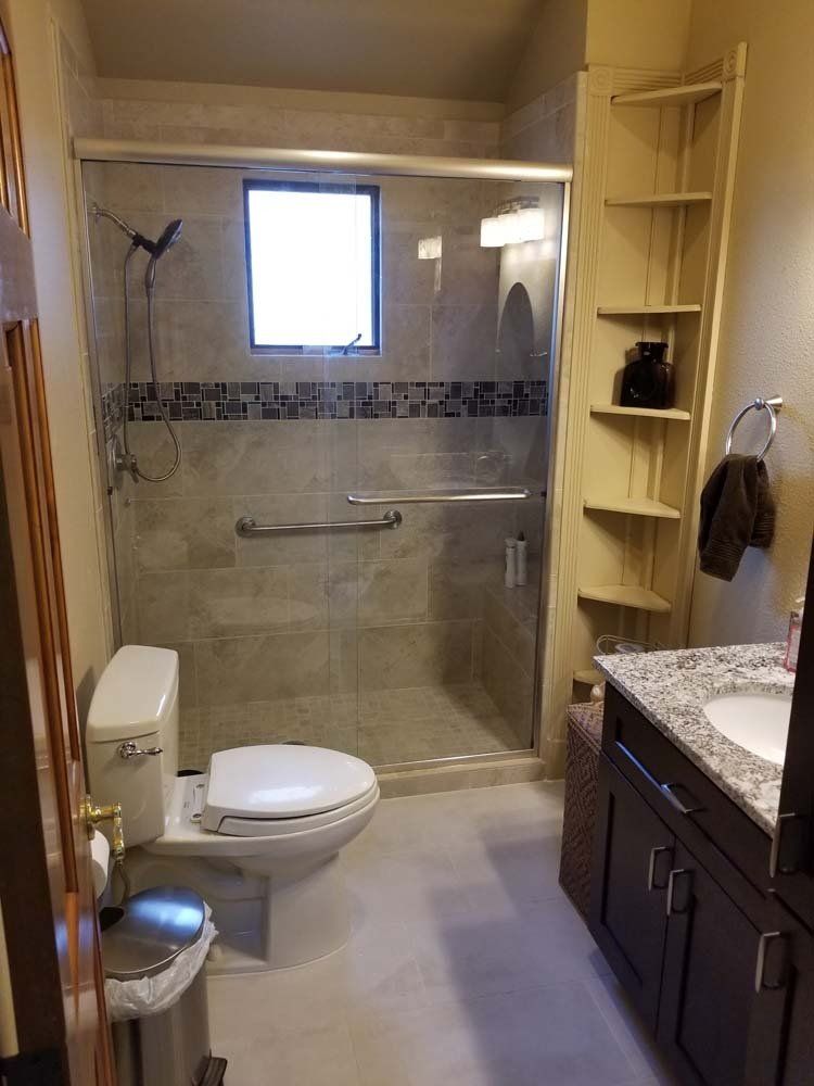 Bathroom with gray tiled shower, toilet, and dark wood vanity; corner shelving.