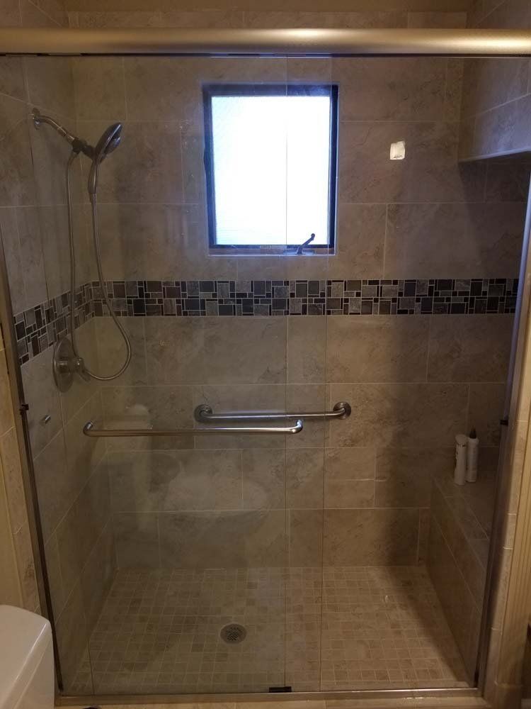Accessible shower with glass door, grab bars, hand shower, and small window above.