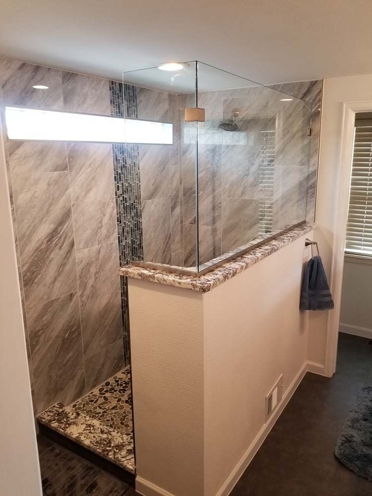 A modern bathroom with a glass shower enclosure, granite countertop, and gray tiled walls.