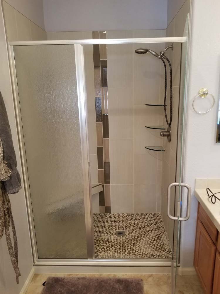A walk-in shower with frosted glass door, pebble floor, and neutral tile walls.
