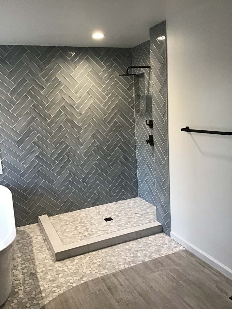 Gray tiled walk-in shower with herringbone pattern, black fixtures, and a step-up entry.