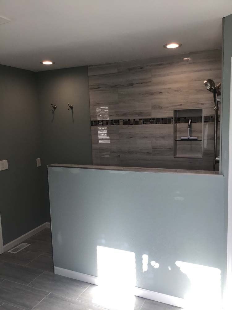 Modern bathroom with gray walls, tiled shower, and a low blue wall.