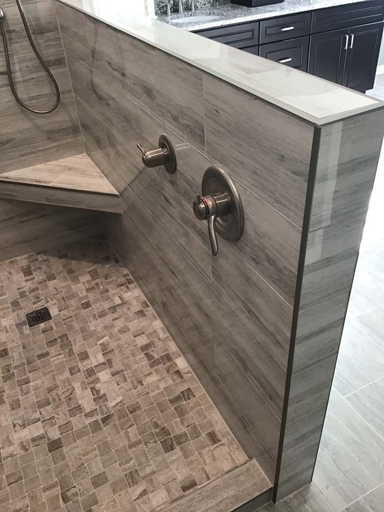 Shower with gray wood-look tile on the walls, bench, and floor. Bronze-toned fixtures.
