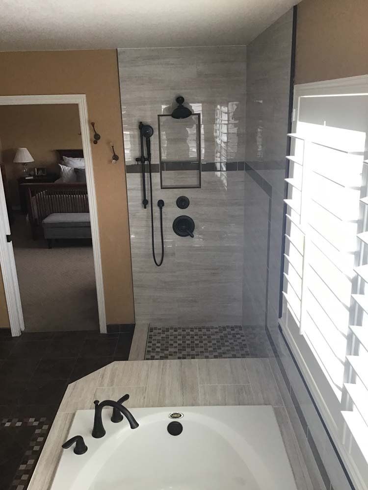 Bathroom with a tub and a tiled shower, black fixtures, and a window with white shutters.