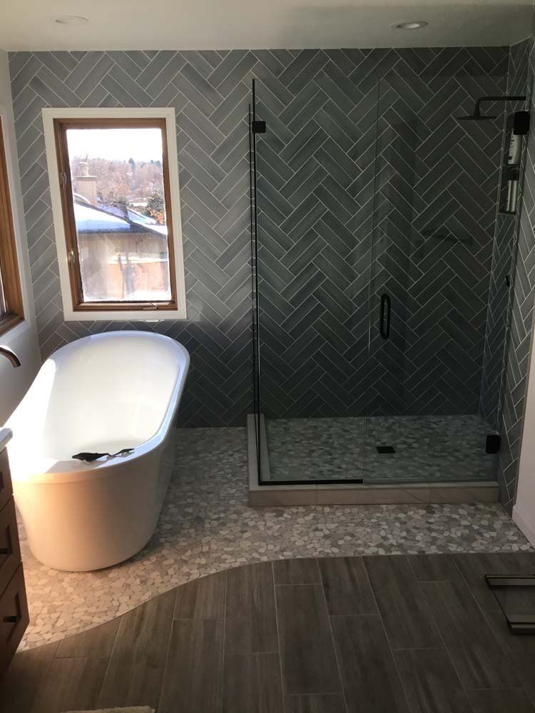Modern bathroom with freestanding tub, tiled shower, herringbone tile wall, wood-look floor.