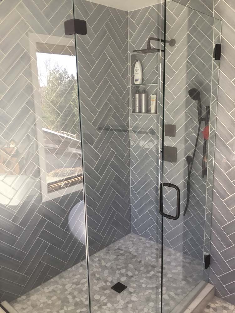 Gray tiled shower with glass doors and a pebble floor.