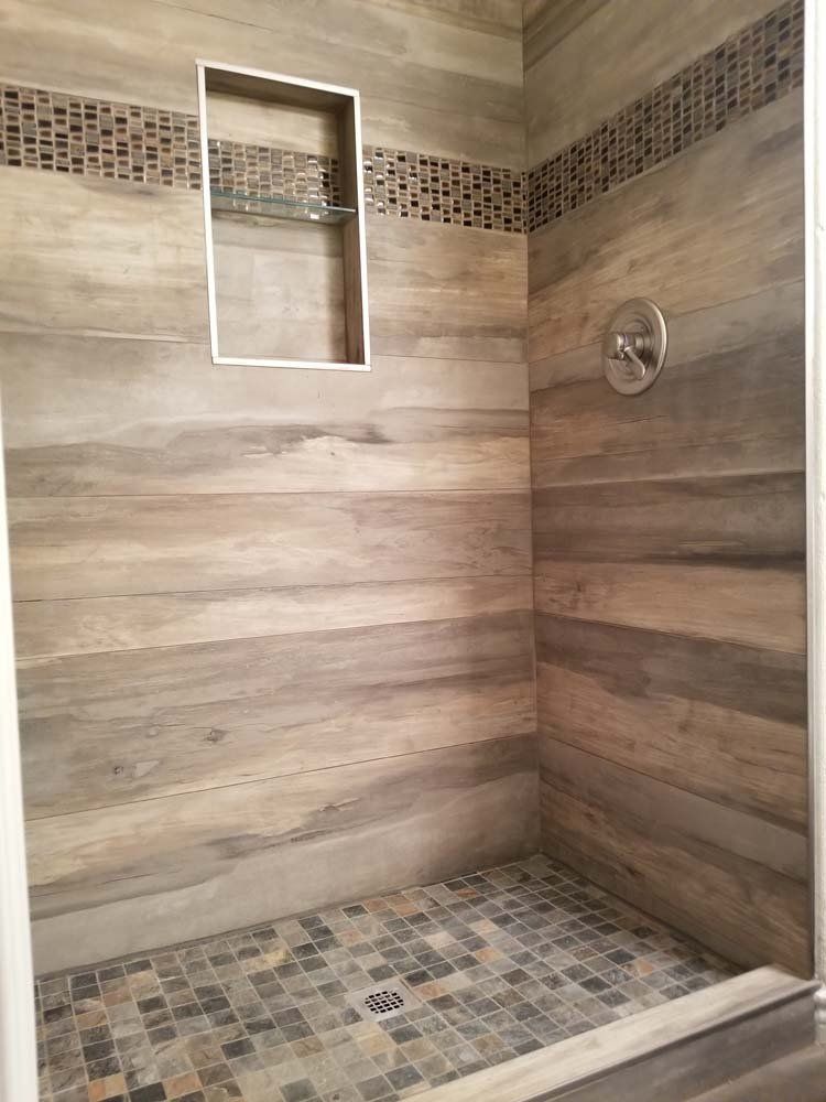 Tiled shower stall with a wood-look wall tile and a mosaic tile shower floor. Includes a built-in shelf.