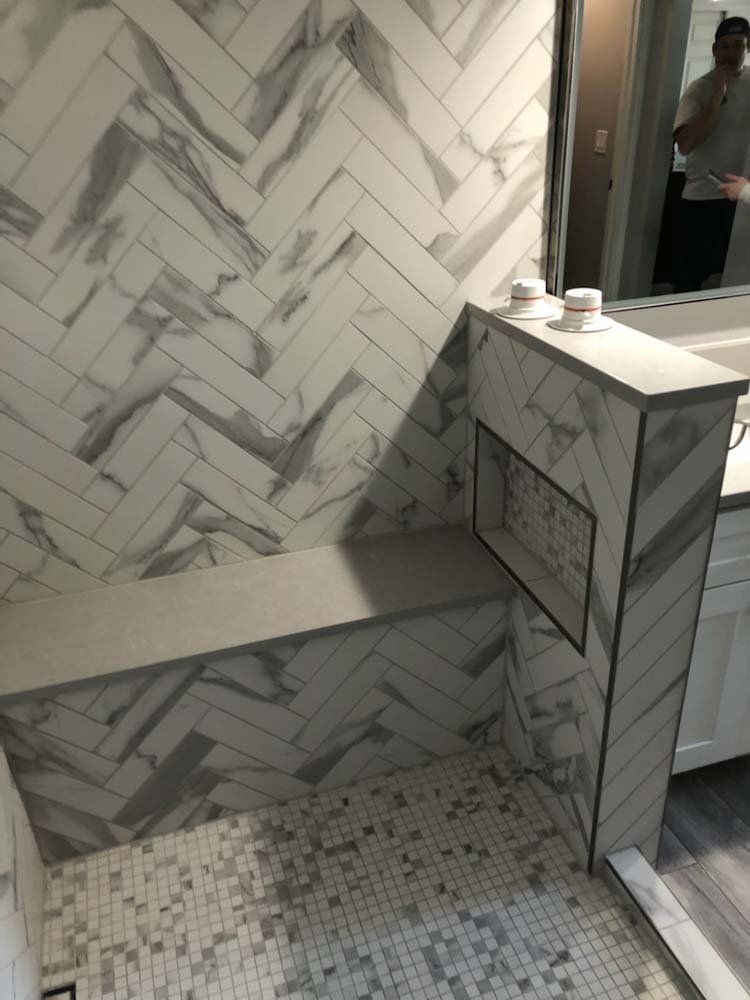 Herringbone tiled shower with built-in bench and niche. Gray and white marble look.