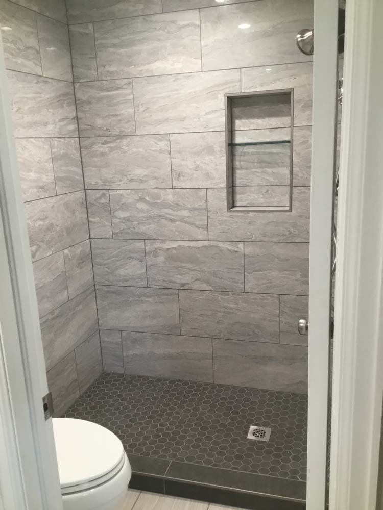 Bathroom with gray tiled shower and dark gray hexagon tile floor, a built-in shelf, and a toilet.