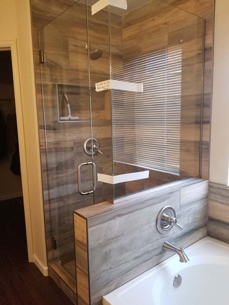 Corner shower with glass door and tile walls, attached to a bathtub.