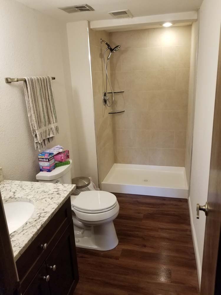 Bathroom with dark wood floors, white shower and toilet, granite countertop, and towel rack.