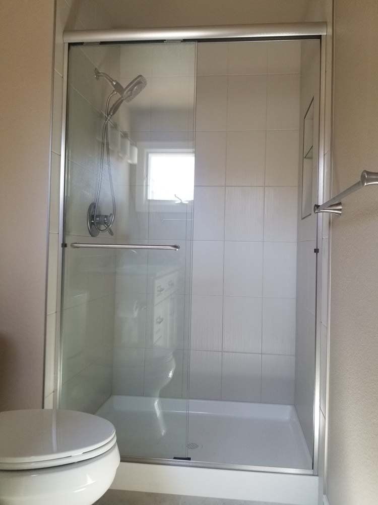 Shower with glass sliding door and white tile.