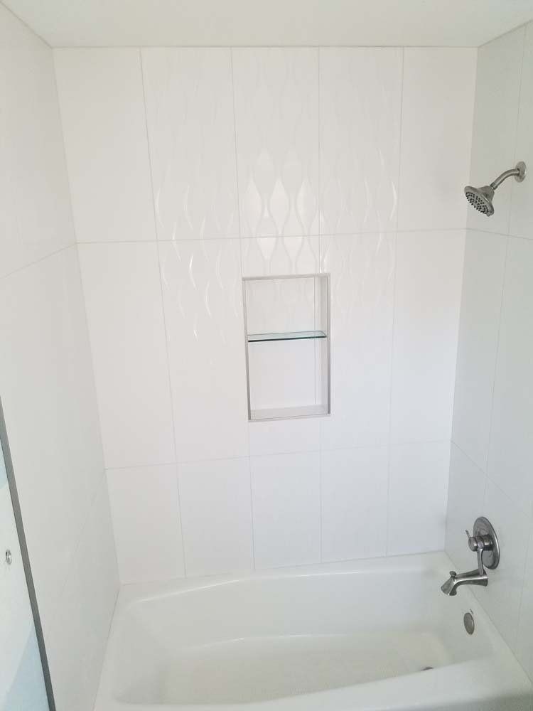 White tiled shower with built-in shelf, bathtub, and chrome showerhead.