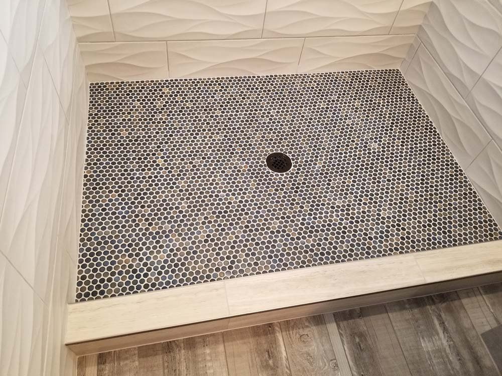 Shower with a tiled floor and walls. The floor has small, dark hexagonal tiles and a drain.
