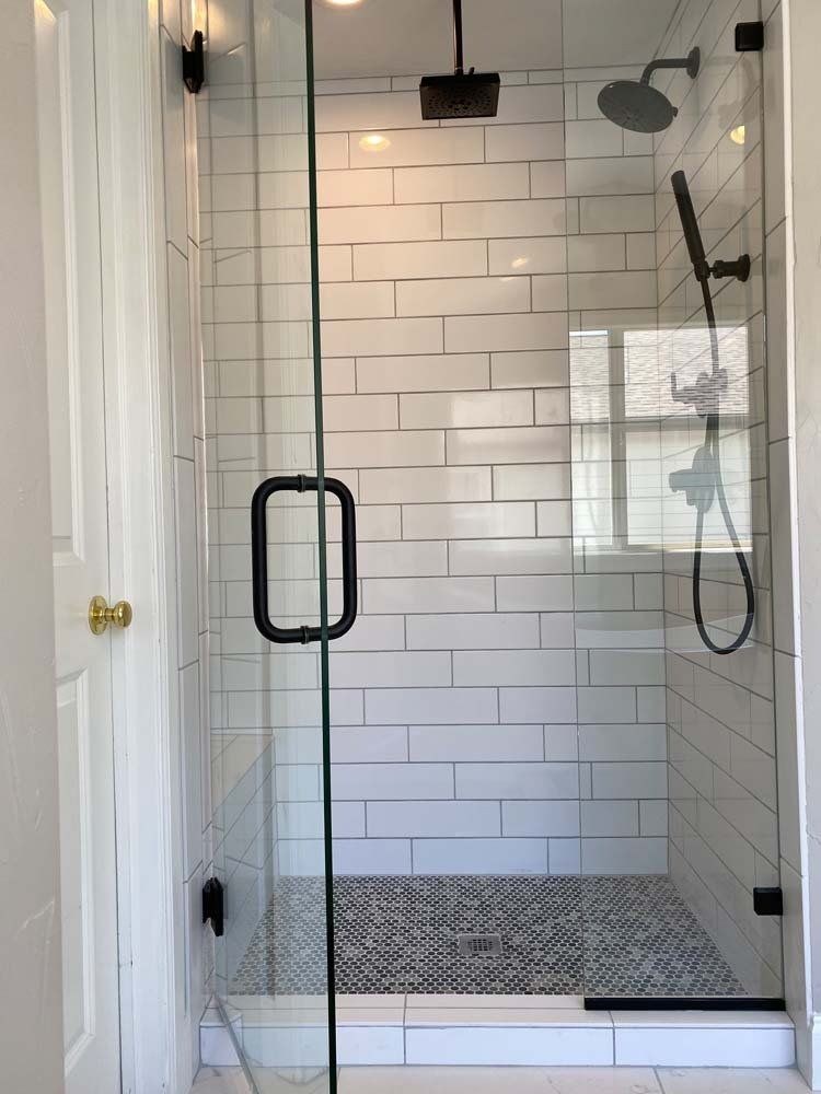 Glass-walled shower with white subway tile, black and white floor, and black fixtures.