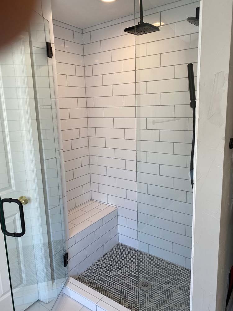 Shower stall with white subway tiles, dark fixtures, glass door, and pebble tile floor.