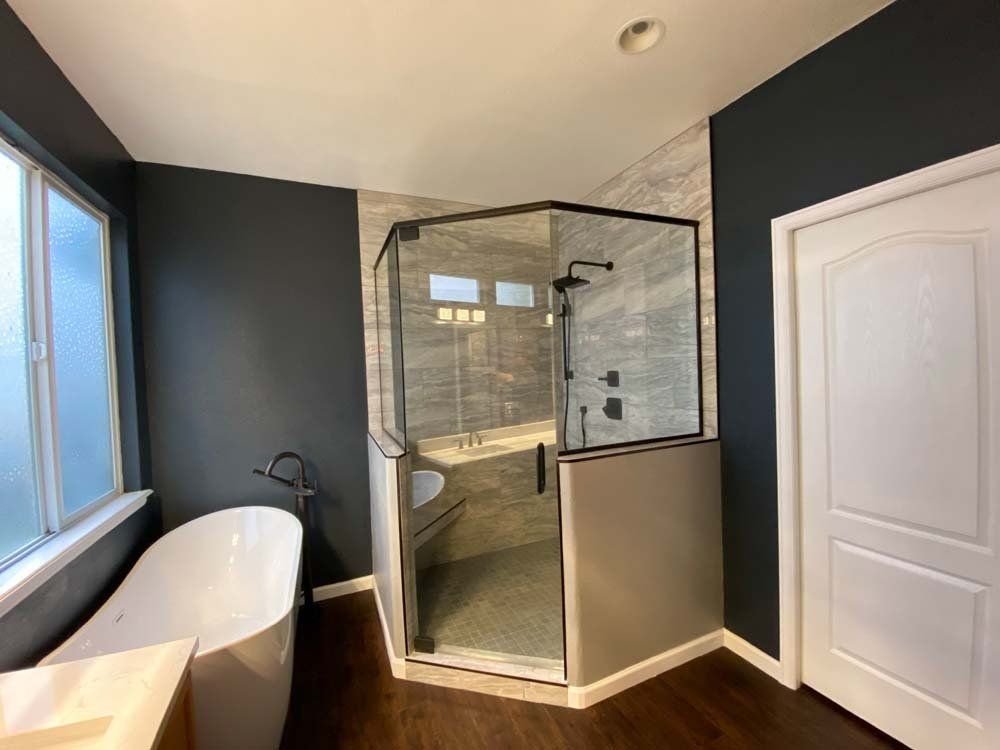 Modern bathroom with a glass shower, a white bathtub, and dark gray walls.