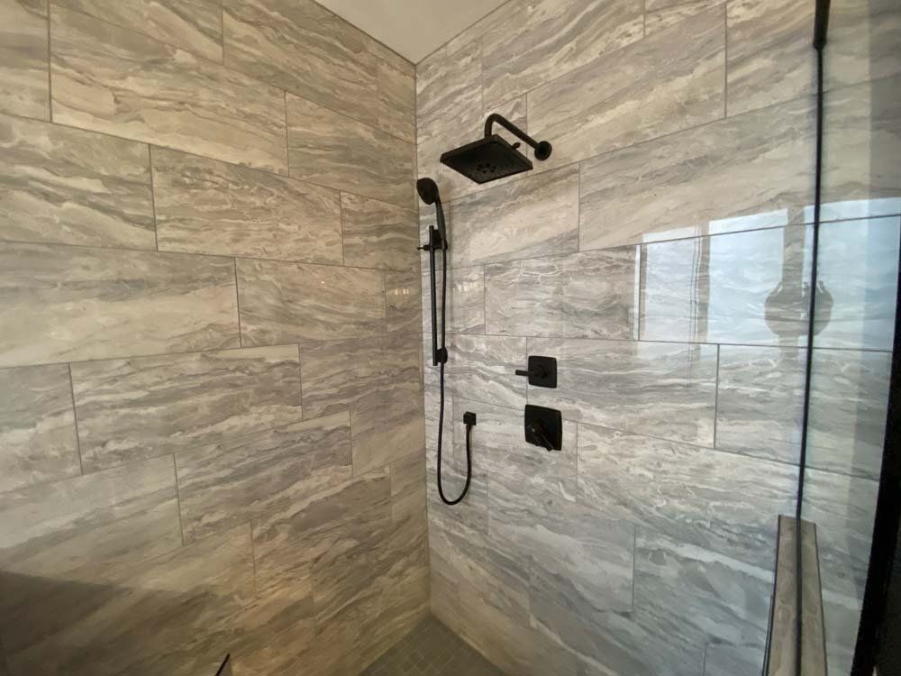 Modern shower with grey stone tiles, black fixtures, and glass door.