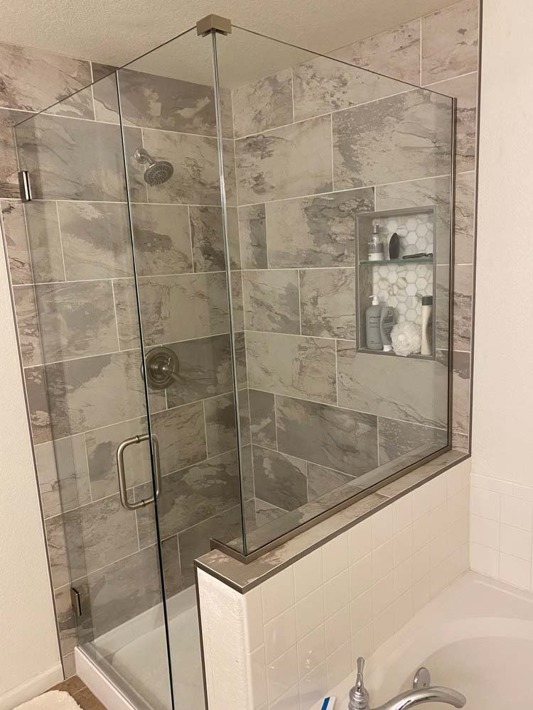 Glass shower enclosure with gray tiled walls and a built-in shelf.