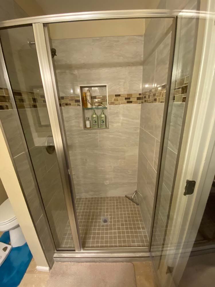Shower stall with glass doors, tiled walls in neutral tones, and built-in shelf.