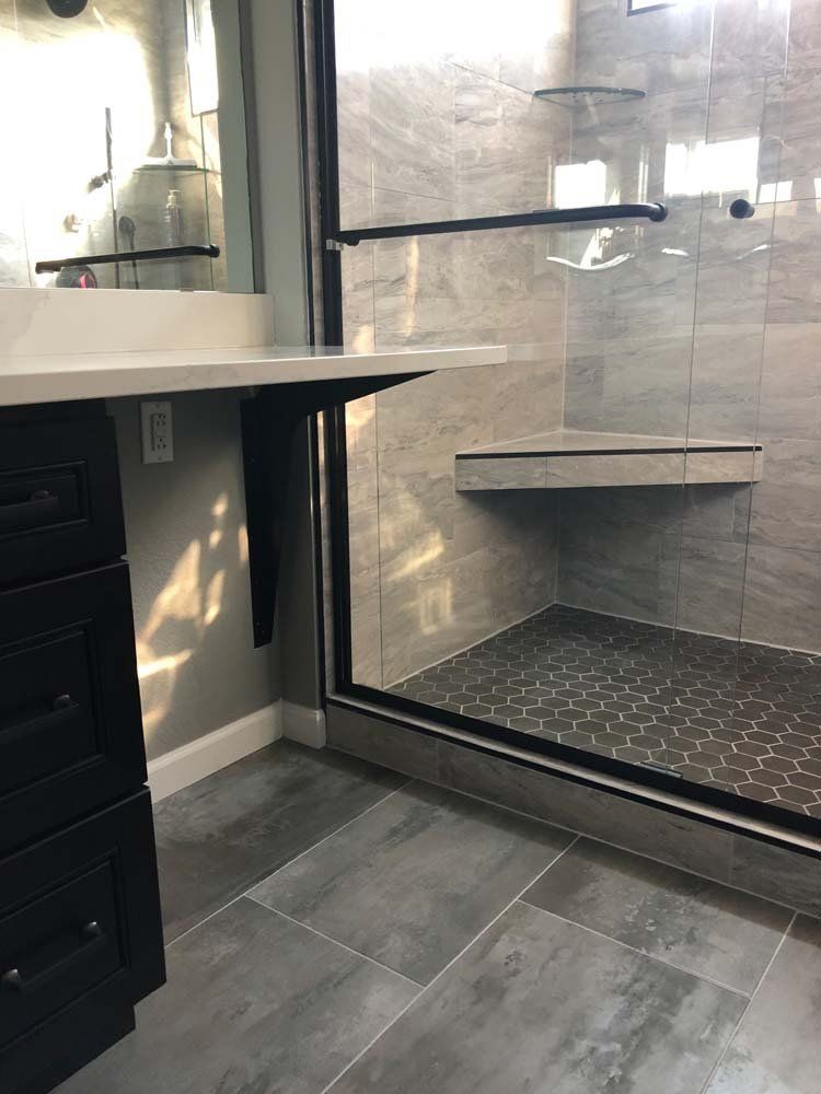 Bathroom with black cabinets, gray tile, and a glass shower.