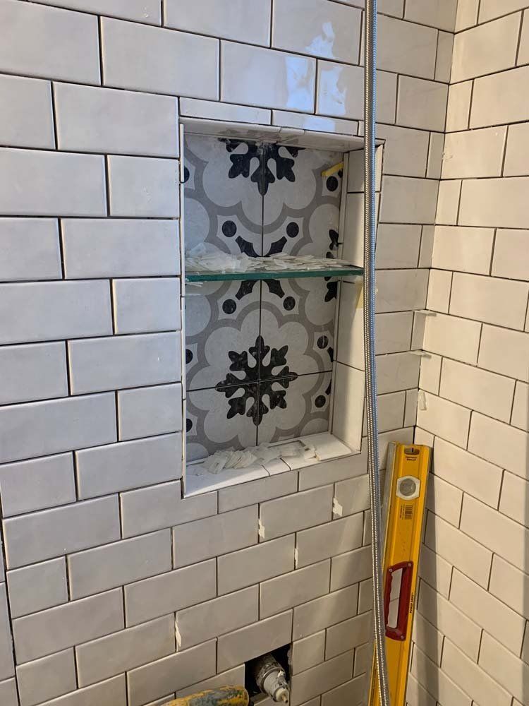 Bathroom shower niche with patterned tile back and glass shelf, surrounded by white subway tiles.