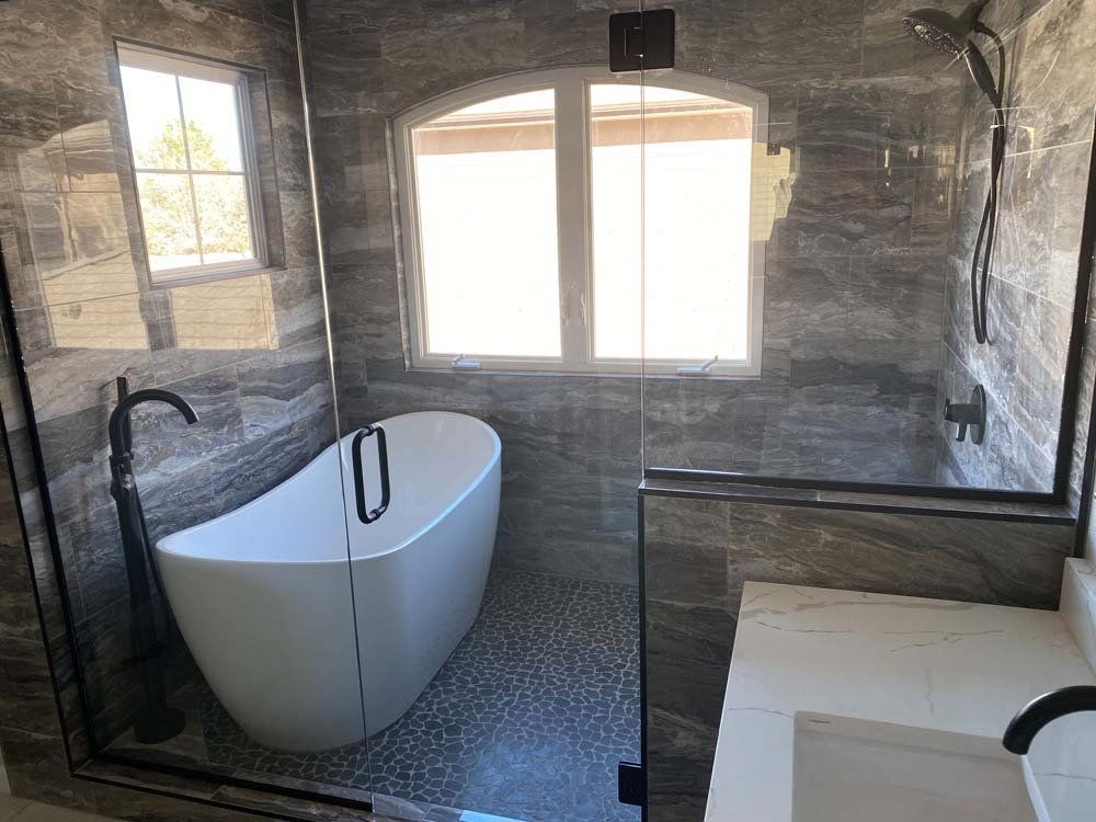 Bathroom with freestanding tub, tiled walls, large window, and glass shower enclosure.