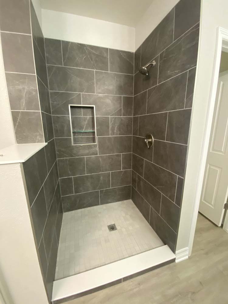 Dark tiled shower with a niche and shower fixtures; light gray floor.