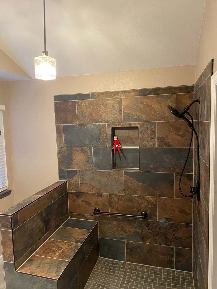 Shower with stone tile walls, built-in bench, black fixtures, and a recessed shelf holding an Elf on the Shelf.