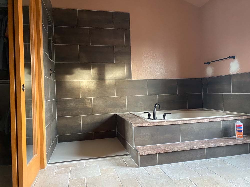 Bathroom with dark tiled walls, raised tub area, and step, featuring a shower stall and light-colored flooring.