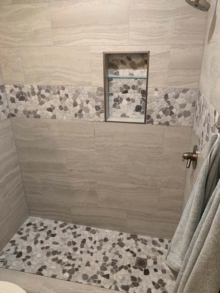 Shower with light gray and pebble tile. A recessed shelf is in the wall. Towels hang on the right.