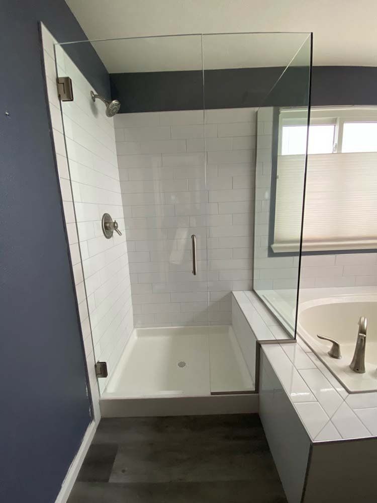 Shower with glass doors and white tile, next to a bathtub with a window.