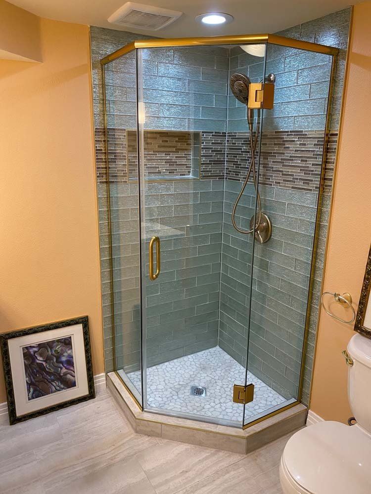 Glass shower with gold trim, blue tile walls, and a white pebble floor.