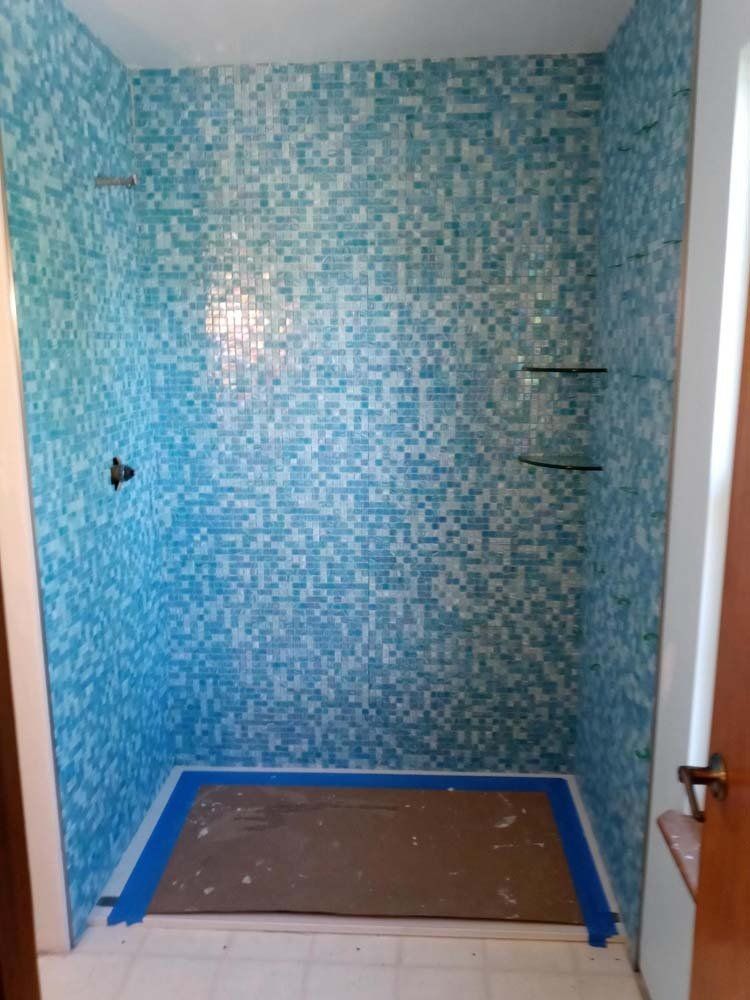 Blue and white tiled shower stall with glass shelves and shower fixtures.