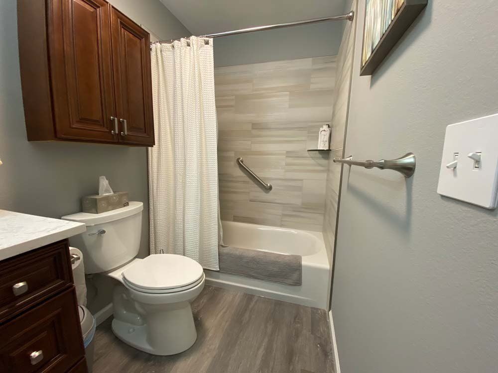 Bathroom with a toilet, shower, wooden cabinets, and gray walls and floor.