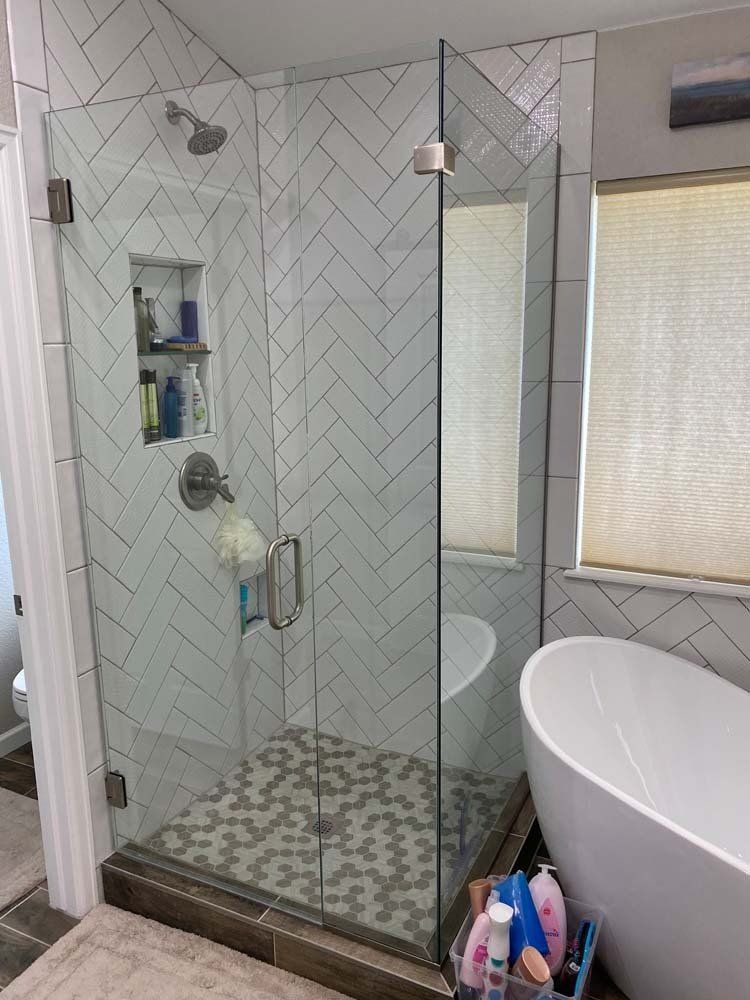 Modern bathroom with glass shower, herringbone tile, and a soaking tub.